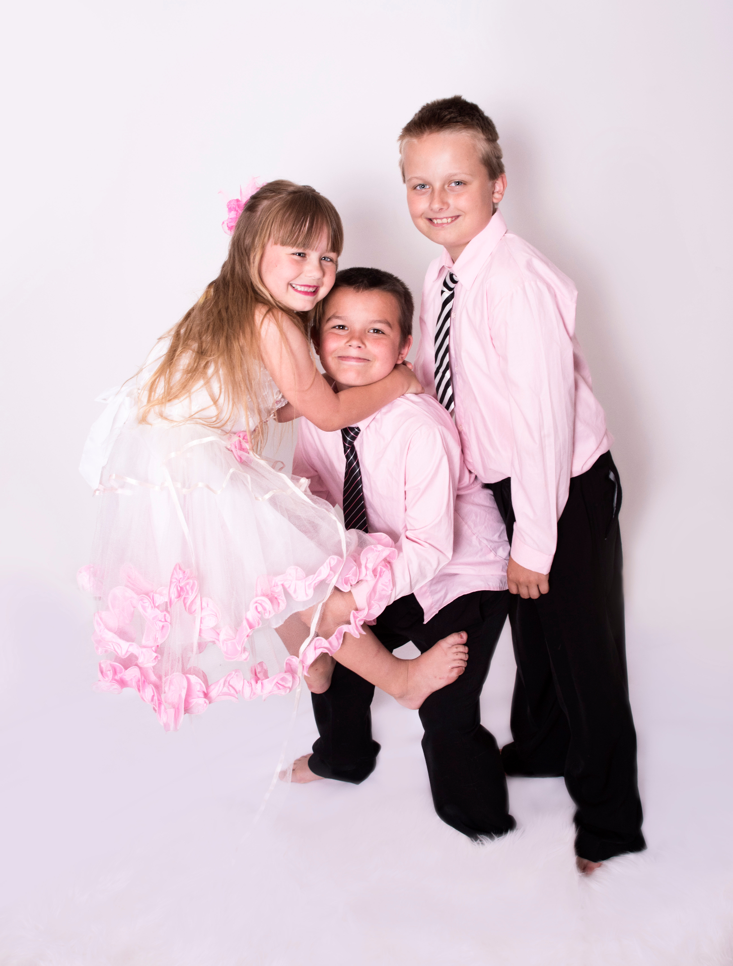 Three siblings dressed in soft pink and black, the little sister in a tulle skirt hugging her two brothers