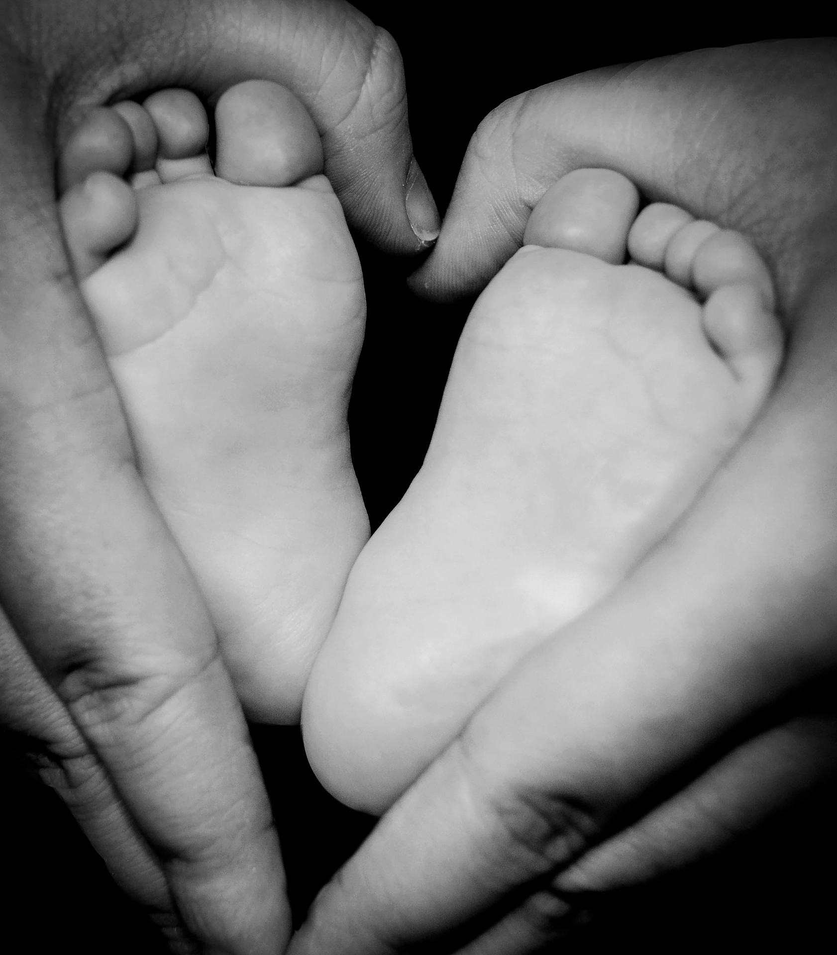 Newborn feet cradled in a parent's hands, black and white studio portrait